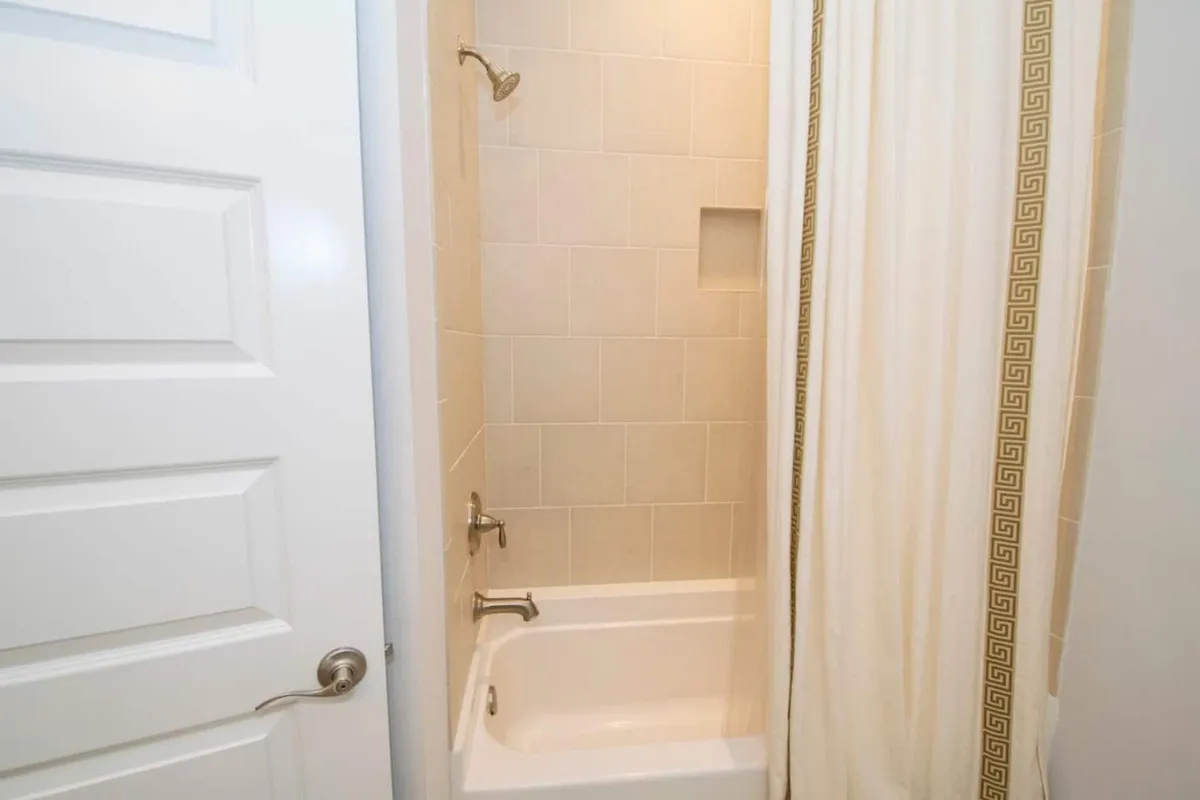 A serene bathroom featuring a combination shower and bathtub, with a light shower curtain and clean, modern wall tiles. The area is bright and tranquil, evoking a spa-inspired ambiance ideal for relaxation and self-care.