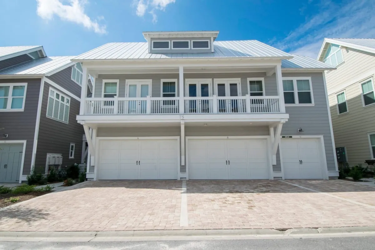 An exterior view of the residence shows three garage doors with carriage-style handles, an upper balcony, and a well-maintained brick driveway. The perspective suggests easy access to the garage, where all your adventure gear is stored.